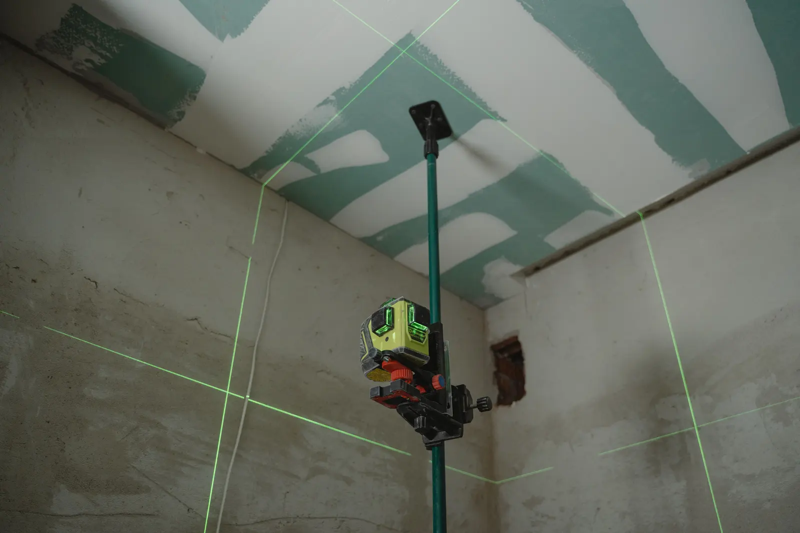 Un niveau laser projette ses lignes vertes sur une cloison en plaques de plâtre.